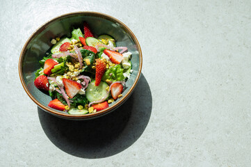 A bowl of salad with strawberries, cucumbers, and onions photographed from above. Room for copy.