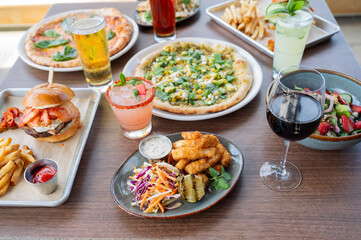 A table full of food including pizza, french fries, and a sandwich. There are also drinks such as beer and a margarita, color photo