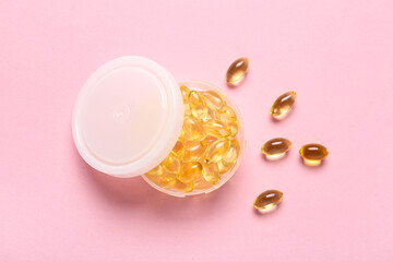 Box with fish oil capsules on pink background