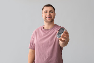 Handsome young happy diabetic man with glucometer on grey background