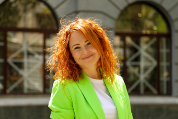 Portrait of a red-haired smiling girl in a light green jacket with slightly curly hair.