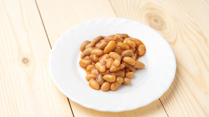 baked beans in sauce on a white plate close-up on a wooden background. the view from the top.