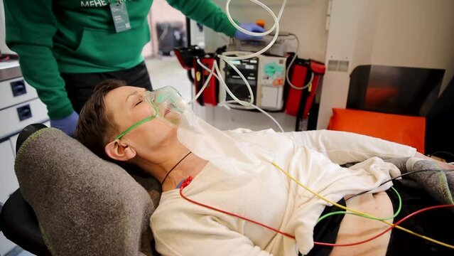 Female patient breathing through oxygen mask. Support in ambulance next to heart rate machine. Mature woman breathing with oxygen air supply