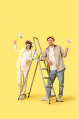 Young couple with paint rollers and stepladder on yellow background. Repair concept
