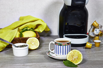 Glass cup with lemon, mint tisane with espresso machine, tea capsule on wood table