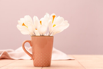 Cup with beautiful white crocus flowers on beige tile table