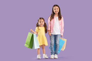 Cute little Asian happy sisters with shopping bags on purple background