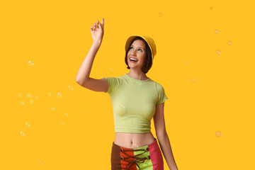 Teenage girl blowing soap bubbles on yellow background