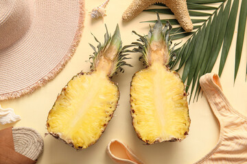 Halves of fresh pineapple with wicker hat, swimsuit, starfish and palm leaf on yellow background