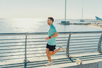 A man jogs along a waterfront path on a sunny day, with the sparkling water in the background.