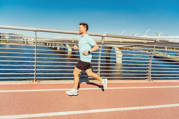 A man in athletic wear jogs along a red path beside a river, with a modern bridge in the background.