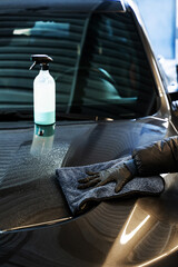 Polishing car body using microfiber cloth. Professional car valeting. Wiping vehicle after applying spray of quick detailer to make car surface clean and shining.