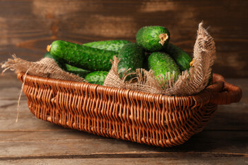 Wicker basket with fresh green cucumbers on wooden background