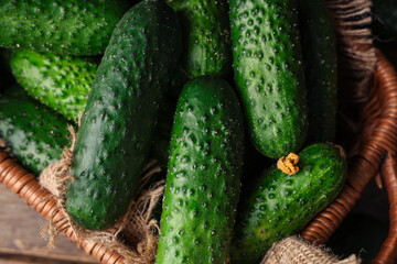 Wicker basket with fresh green cucumbers on wooden background, closeup