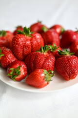 Truskawki na talerzu, na białym obrusie.
