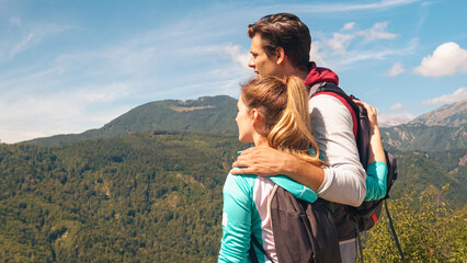 Young, embraced couple enjoying the fantastic mountain and valley panorama, taking a break on a...