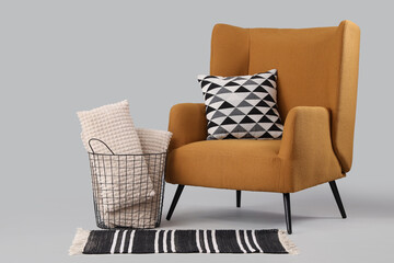 Comfortable armchair with cushions and basket with pillows on grey background