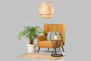 Comfortable armchair with cushion and coffee table with plant on grey background