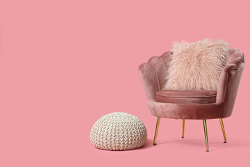 Cozy armchair with fluffy cushion near pouf on pink background