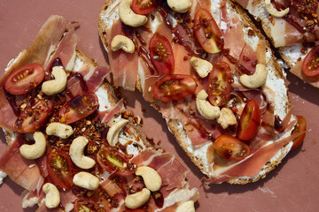 Italian bruschettas with prosciutto, cherry tomatoes, and cashews on a rustic pink surface