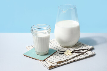 Glass and jug of fresh vanilla milk with sticks and flower on colorful background