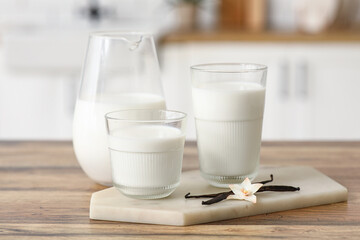 Glasses and jug of fresh vanilla milk with sticks and flower on wooden table in kitchen