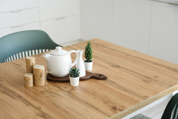 Teapot with plants and candles on dining table in kitchen, closeup