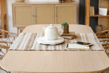 Teapot with tablet computer and books on dining table in room