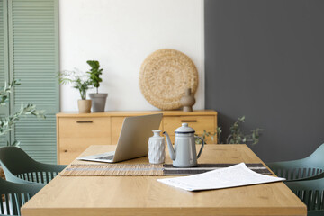 laptop with teapot and newspaper on dining table in room