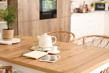 Teapot with notebooks and tablet computer on dining table in kitchen