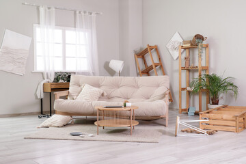 Interior of messy living room with sofa, tables and shelf units