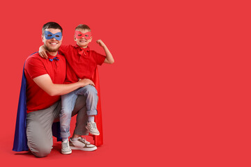 Little boy with his father in superhero costumes on red background