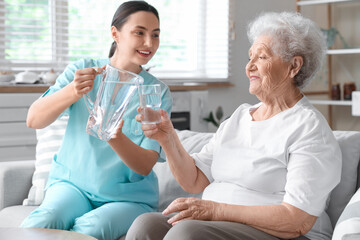 Physical therapist pouring water to senior woman at home - Powered by Adobe