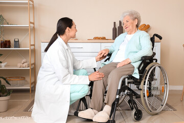 Obraz premium Physical therapist with senior woman in wheelchair holding hands at home