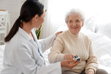 Physical therapist and senior woman with pulse oximeter in bedroom