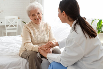 Fototapeta premium Physical therapist with senior woman holding hands in bedroom