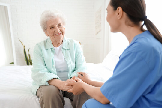 Physical therapist with senior woman holding hands in bedroom