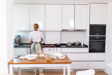 A woman is cooking in a kitchen with white cabinets and a wooden table