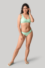 Beautiful young African-American woman in stylish turquoise swimsuit on grey background