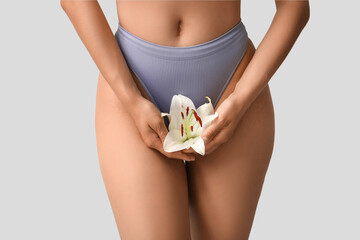 Beautiful young African-American woman in panties with white lily flower on grey background, closeup