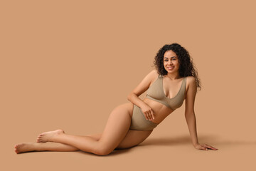 Naklejka premium Beautiful young happy African-American woman in underwear sitting on beige background