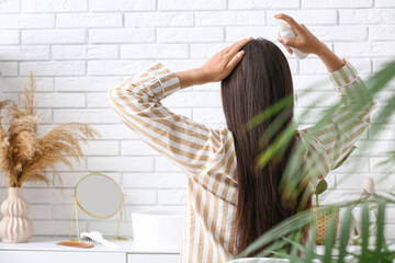 Beautiful young woman with hair spray sitting at home, back view