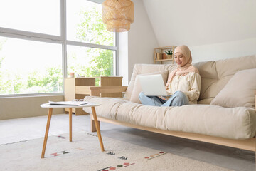 Young Muslim businesswoman working with laptop on sofa at home