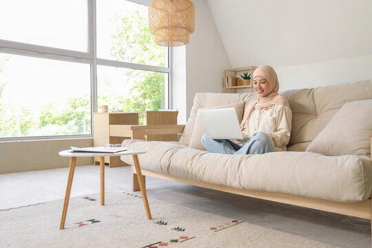 Young Muslim businesswoman working with laptop on sofa at home - Powered by Adobe