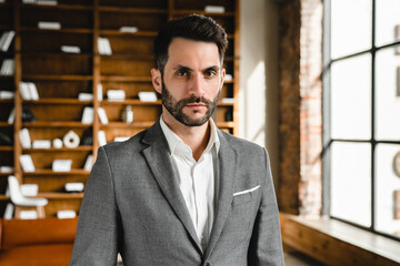 Closeup shot of handsome young businessman wearing formal suit looking at camera in office. Bearded...