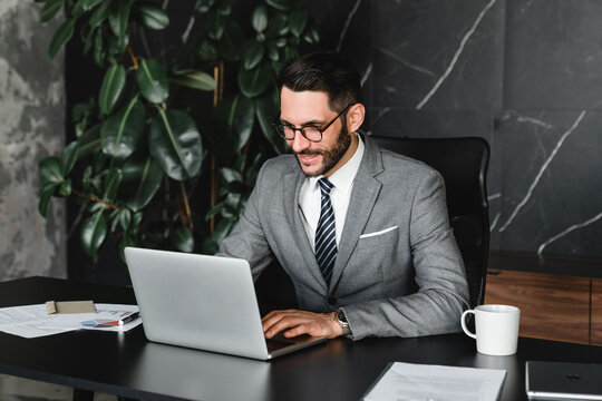 Successful boss typing on laptop remotely in office. Young rich manager businessman checking financial data, doing managerial online job, receiving official letters and e-mails