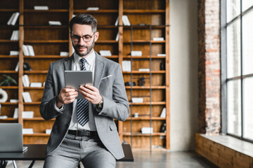 Young successful businessman working on digital tablet while sitting at the desk in office. Foreman...