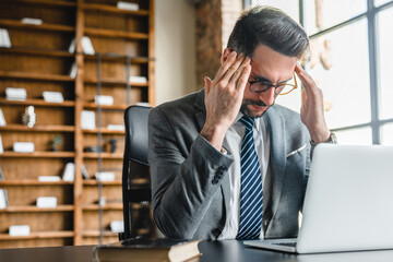 Exhausted young businessman dealing with difficult task working on laptop in office. Tired...