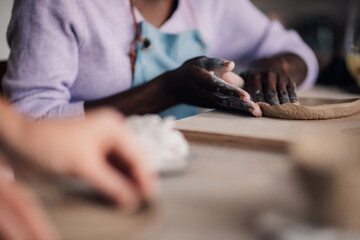 Close up of diverse pottery class attendee's hands making clay plate.