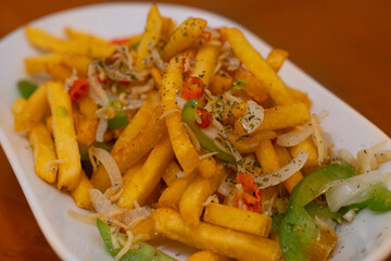 spicy french fries with chilli, garlic, bell pepper, and anchovy toppings, served on white long plate on wooden table surface